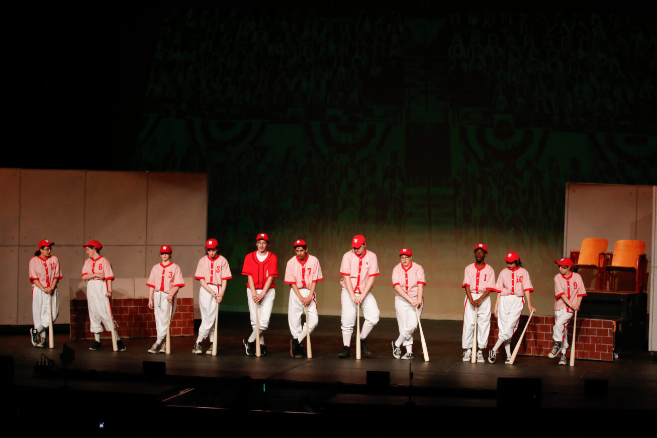 The cast members portraying the Washington Senators baseball team stand on stage in their uniforms