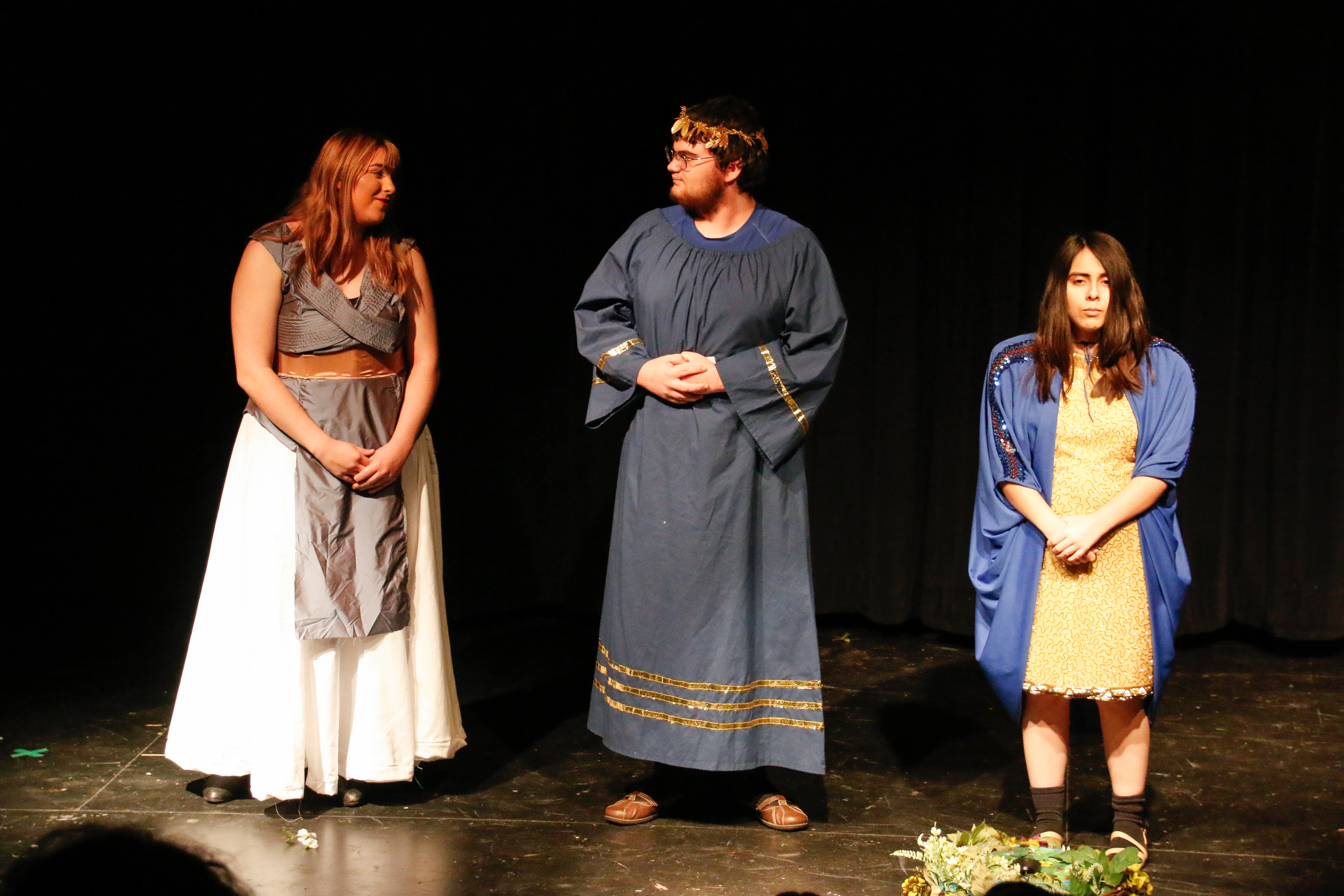 Three student actors stand on stage in their Shakespearean costumes