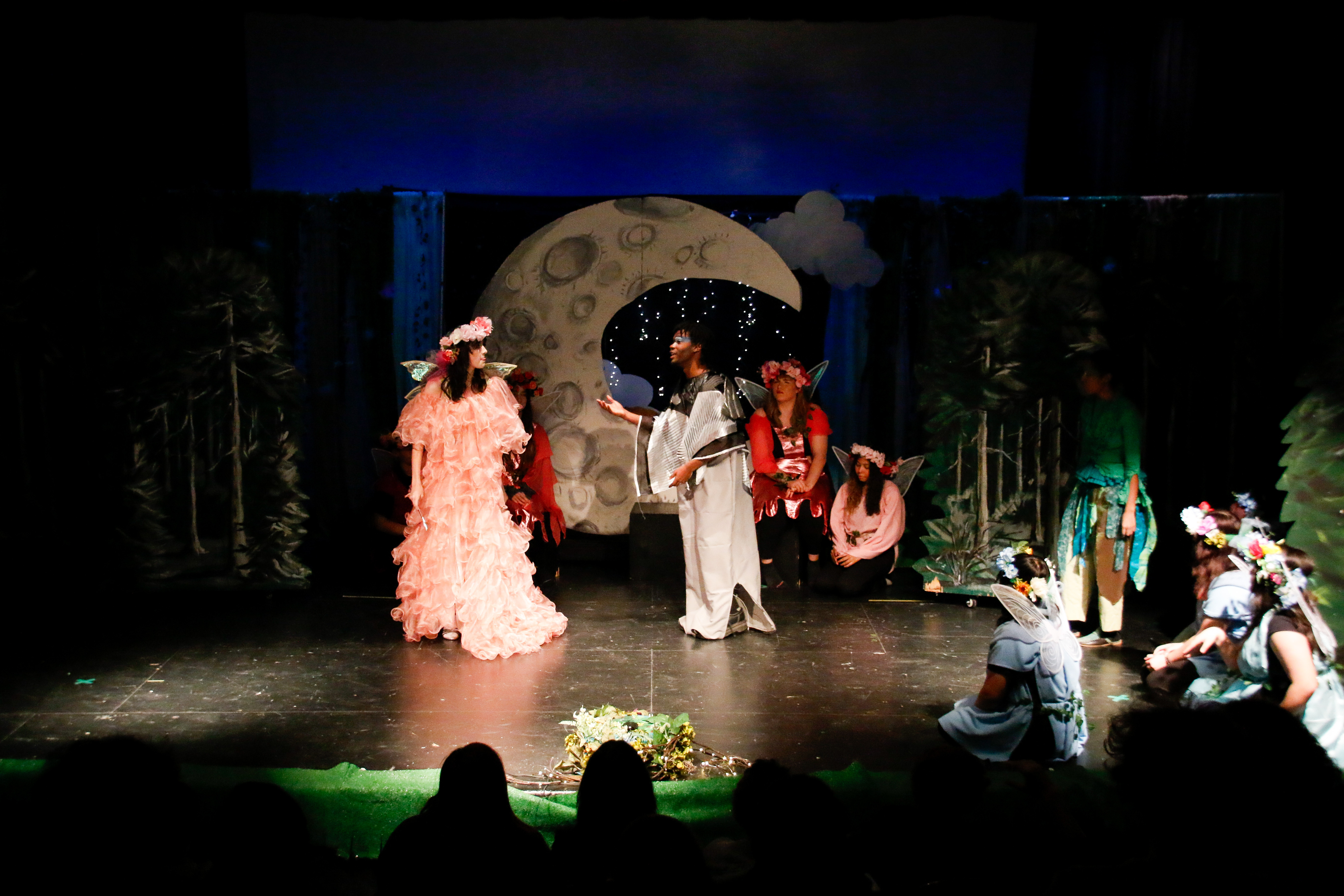 Student actors stand on stage in front of a cutout of the moon