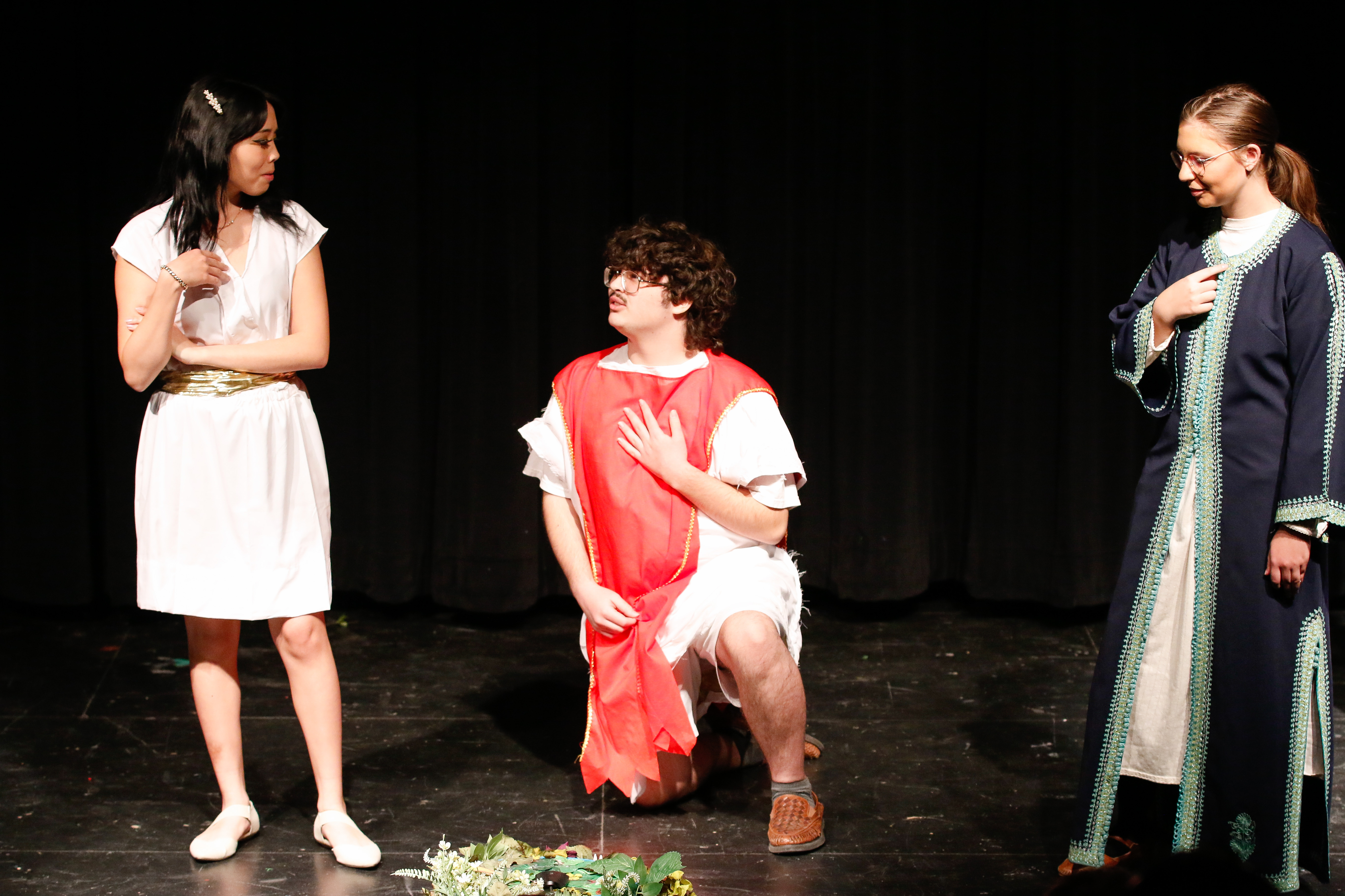 Three student actors stand on stage in their costumes