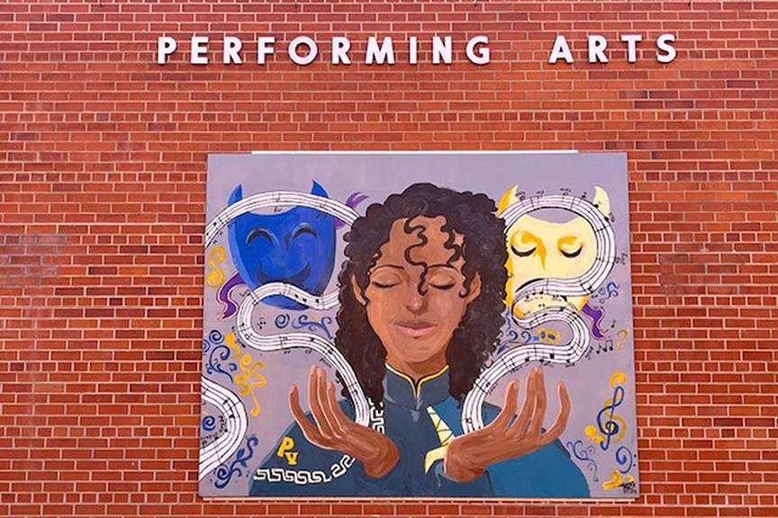 An arts themed mural under the Performing Arts sign on a brick wall