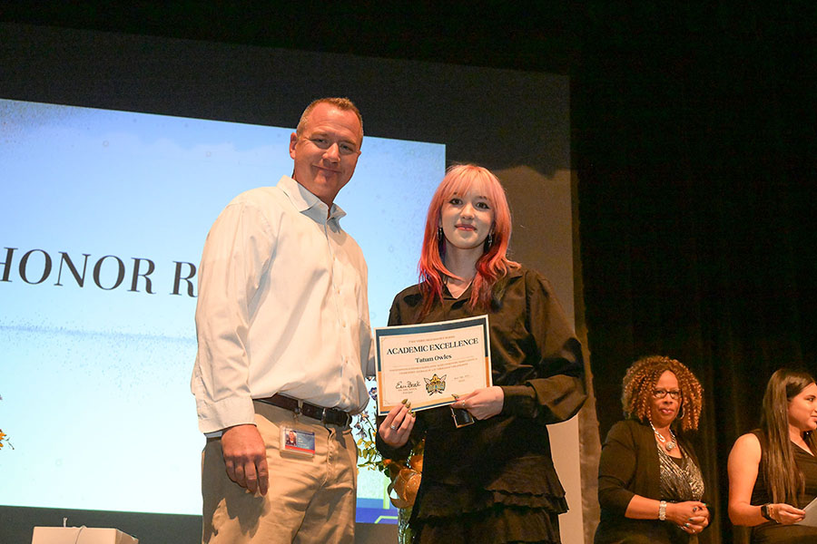 The principal smiles with a teen girl with pink hair, holding an award certificate