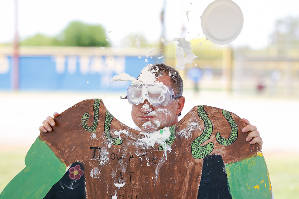 A man wearing goggles gets a pie thrown at his face