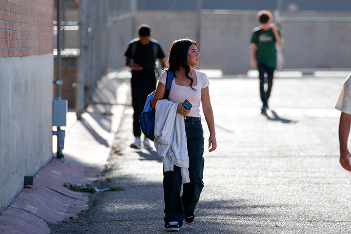 A teen girl holds a hoodie over her arm and looks off to the right as she walks across campus