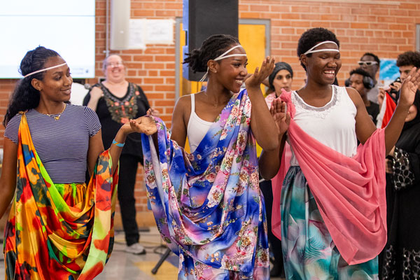 Students dressed in colorful outfits dance in front of a crowd.