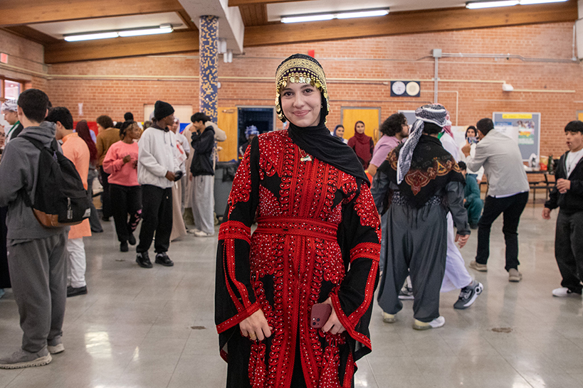 A young woman smiles in her traditional dress and coin headscarf