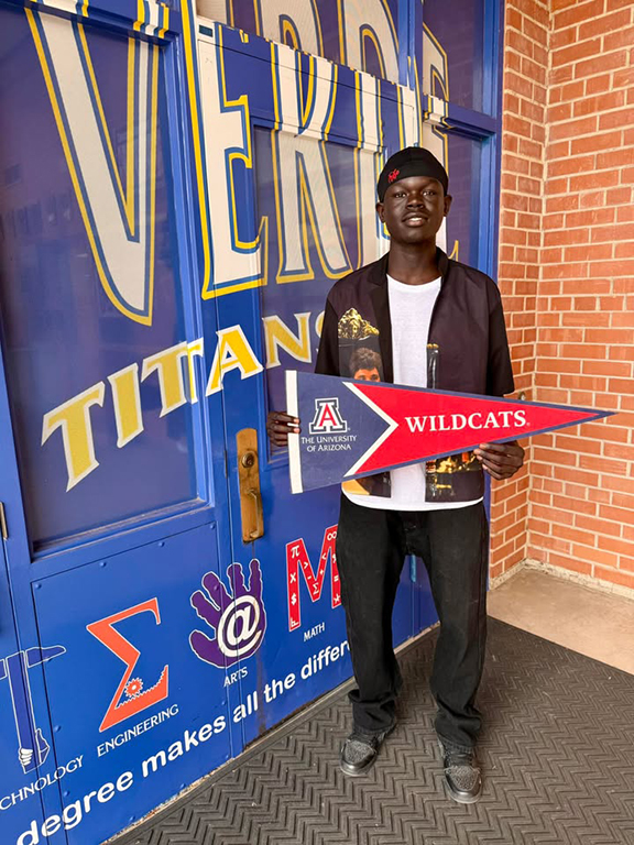 A teen boy smiles holding a UofA Wildcats pennant