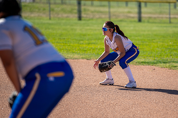 A girl squats on the softball field, getting ready to catch the ball