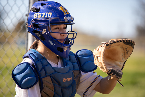 A girl in catchers gear holds up her glove to catch the softball