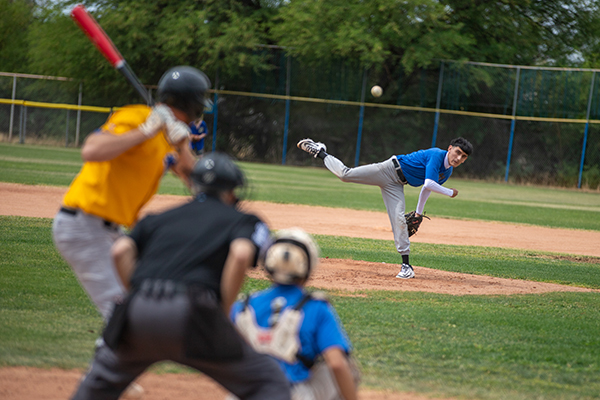 A teen boy in a blue jersey throws out a pitch