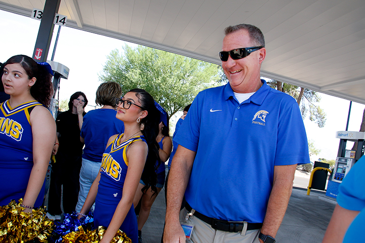 A man in a blue shirt and sunglasses laughs, with two girls in blue and yellow cheer uniforms next to him