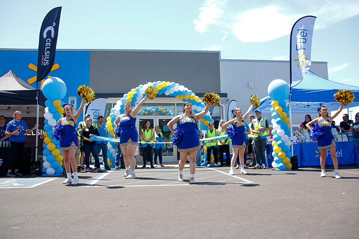 Cheerleaders perform a pom routine in front of a blue, yellow and white balloon arch