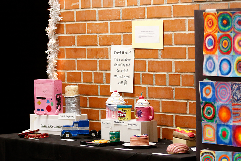 A display of ceramic artwork, including replicas of a plate of pancakes, a can of Play-Doh, a mug of hot cocoa, a burrito and a semi truck
